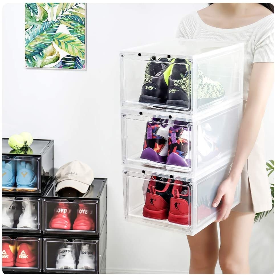 A person holding three storage bins with shoes in them