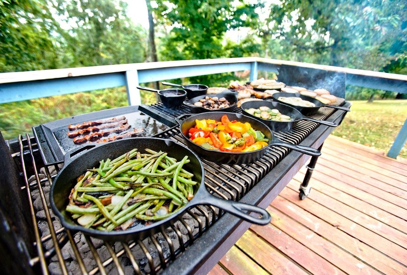 lots of cast iron skillets cooking vegetables while on a grill