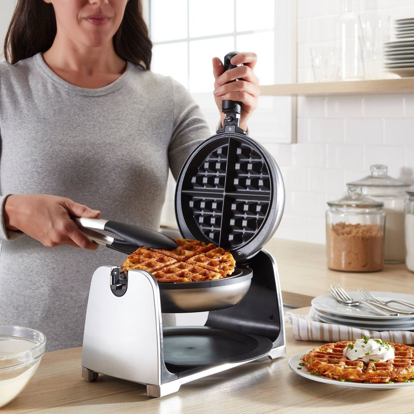 person using tongs to lift up a cooked waffle from a flipped waffle maker