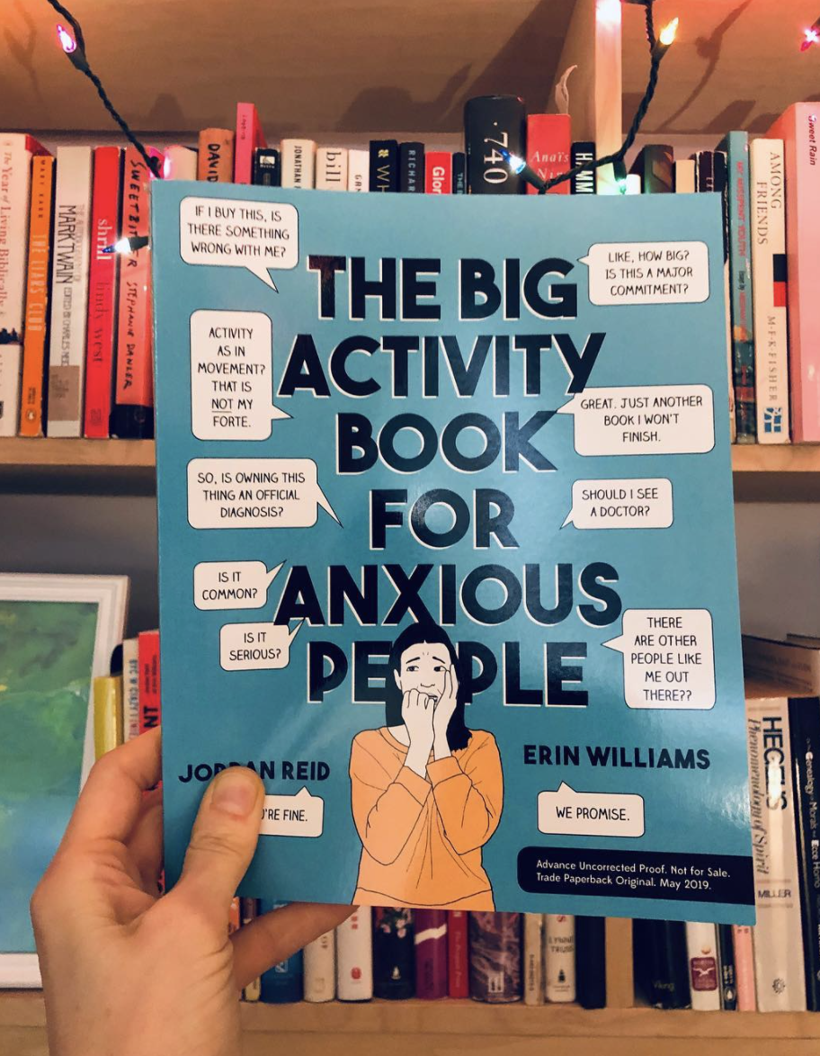 hand holding The Big Activity Book for Anxious People in front of a bookshelf