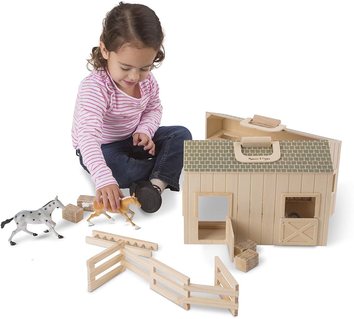 A child plays with a toy stable with two toy horses