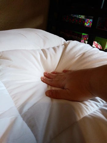A reviewer showing how squishy the mattress topper is by pressing down on it