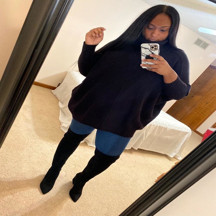 Reviewer wears black over-the-knee suede boots with a cozy black sweater and jeans