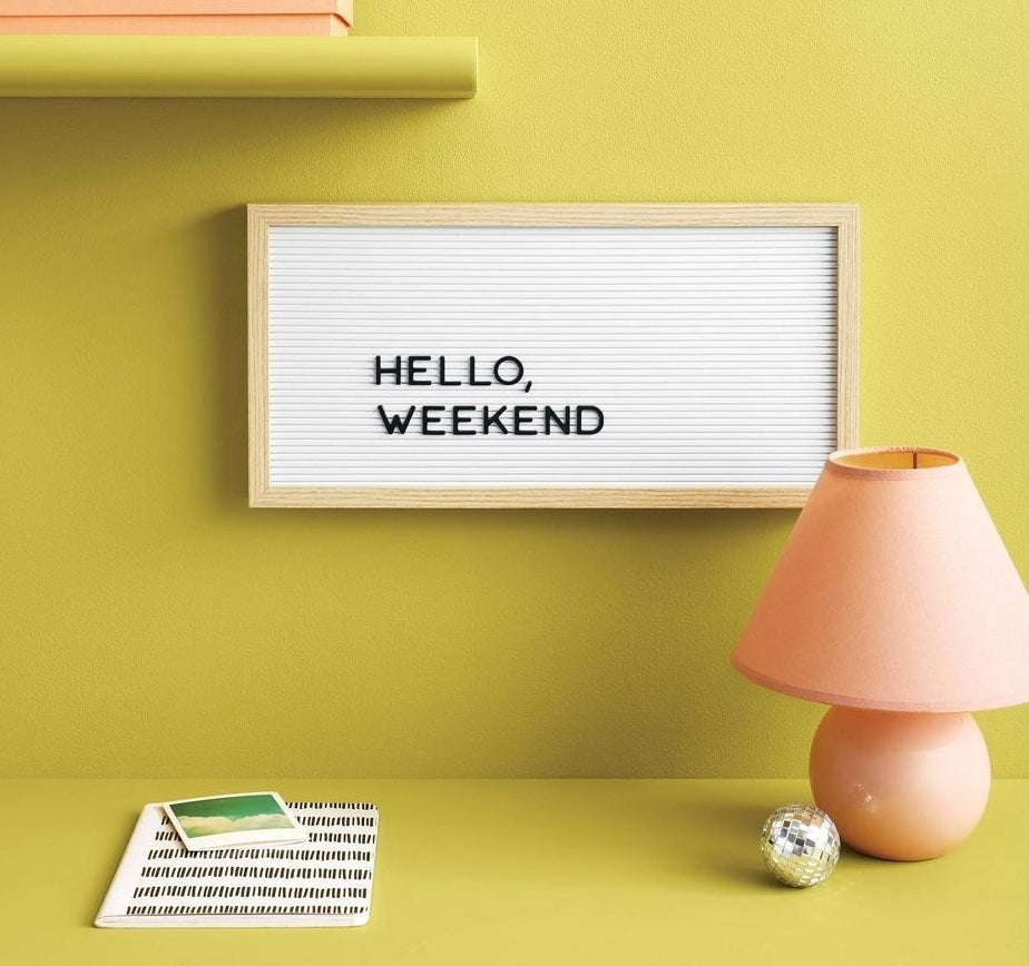 long letterboard with the saying "hello weekend" hung up on a yellow-green wall