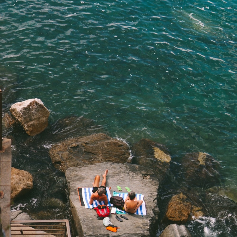 Top down shot of people sitting on a rock sunbathing next to the ocean