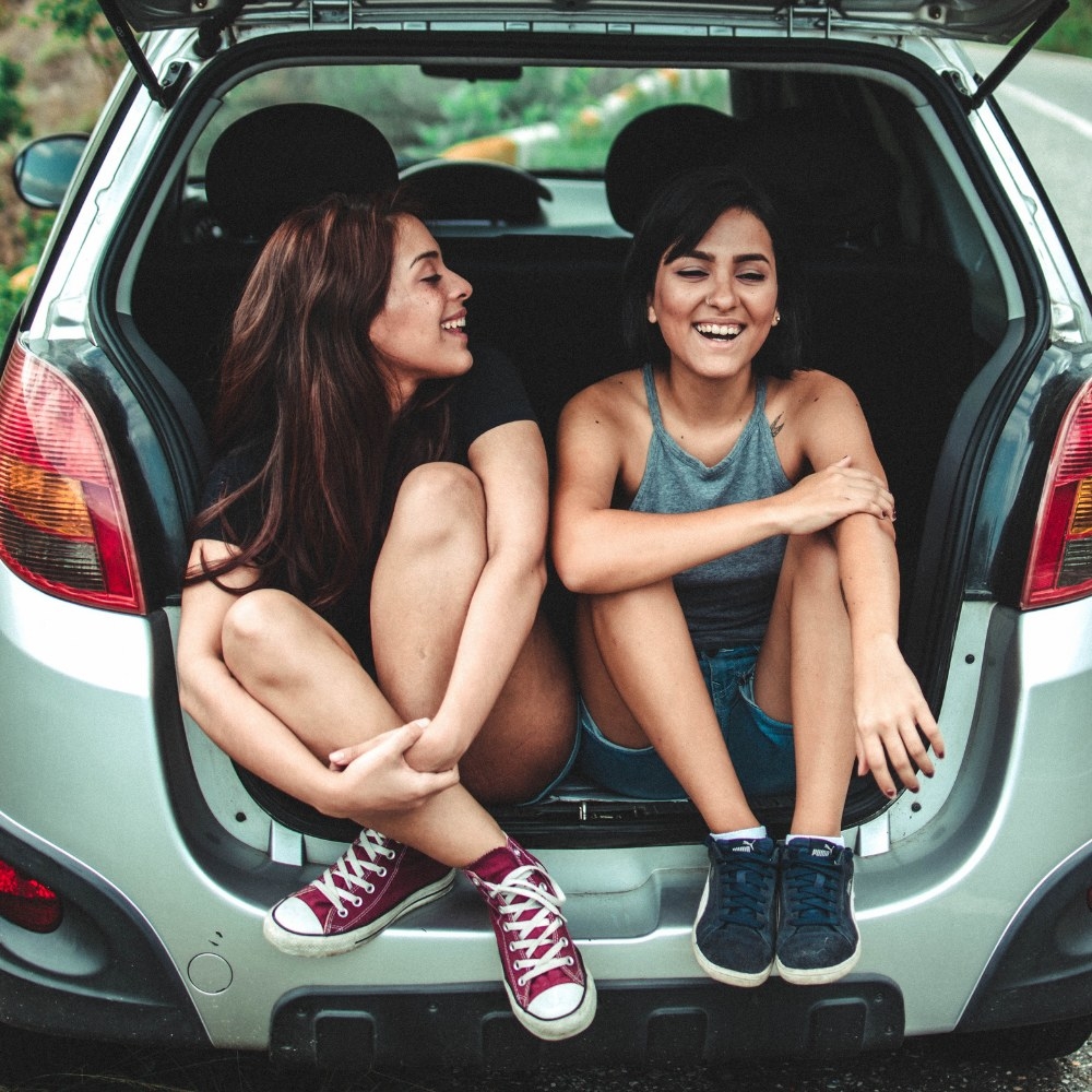 Two girls sitting in a boot smiling and chatting to each other