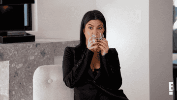 Kourtney Kardashian sips on her drink as she leans back in her chair and looks around, wide-eyed, on Keeping Up With The Kardashians