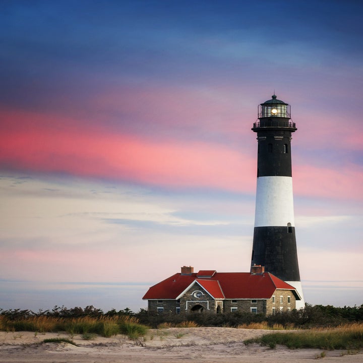 A colorful sunrise scene with a distinct pink stripe against the Fire Island Lighthhouse