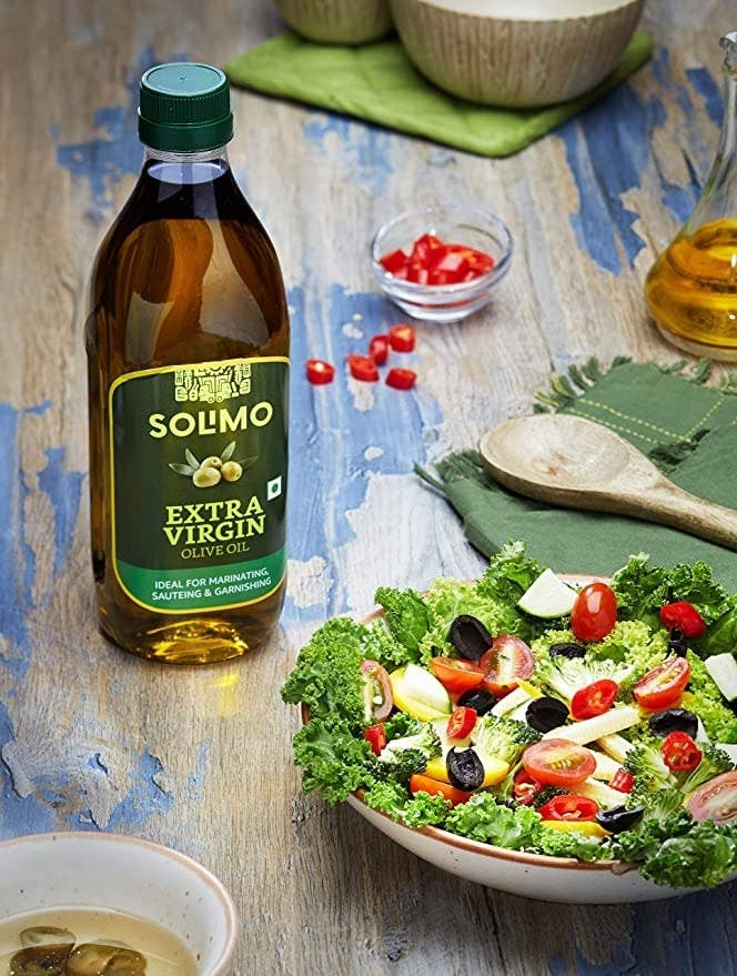 Bottle of olive oil on a wooden table next to a bowl of salad.