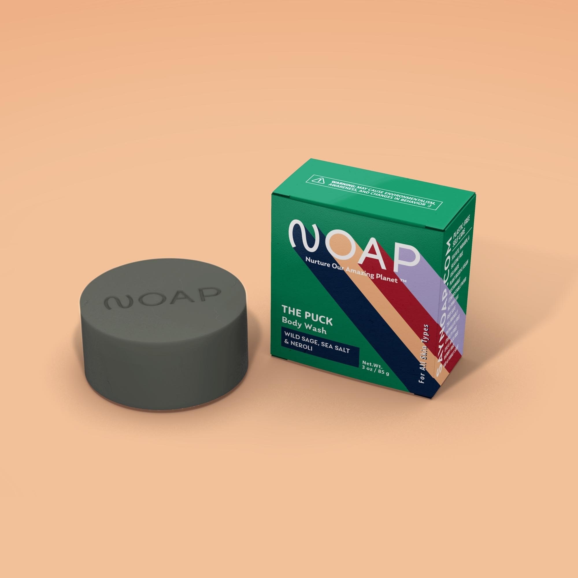 a puck-like gray bar of soap with "noap" etched into it next to a green box with the logo on it