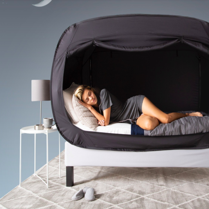 a model laying in a bed surrounded by a gray privacy pop tent 