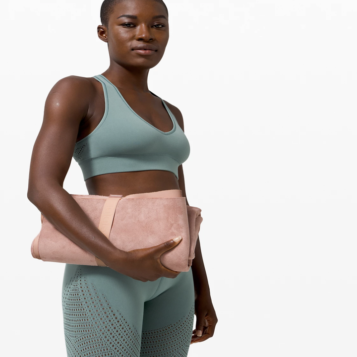 Model holding the pink yoga mat with a pink strap holding it together, showing how it folds up to be the size of a medium clutch