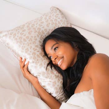 A model putting their head on a pillow with the leopard print satin pillowcase over it