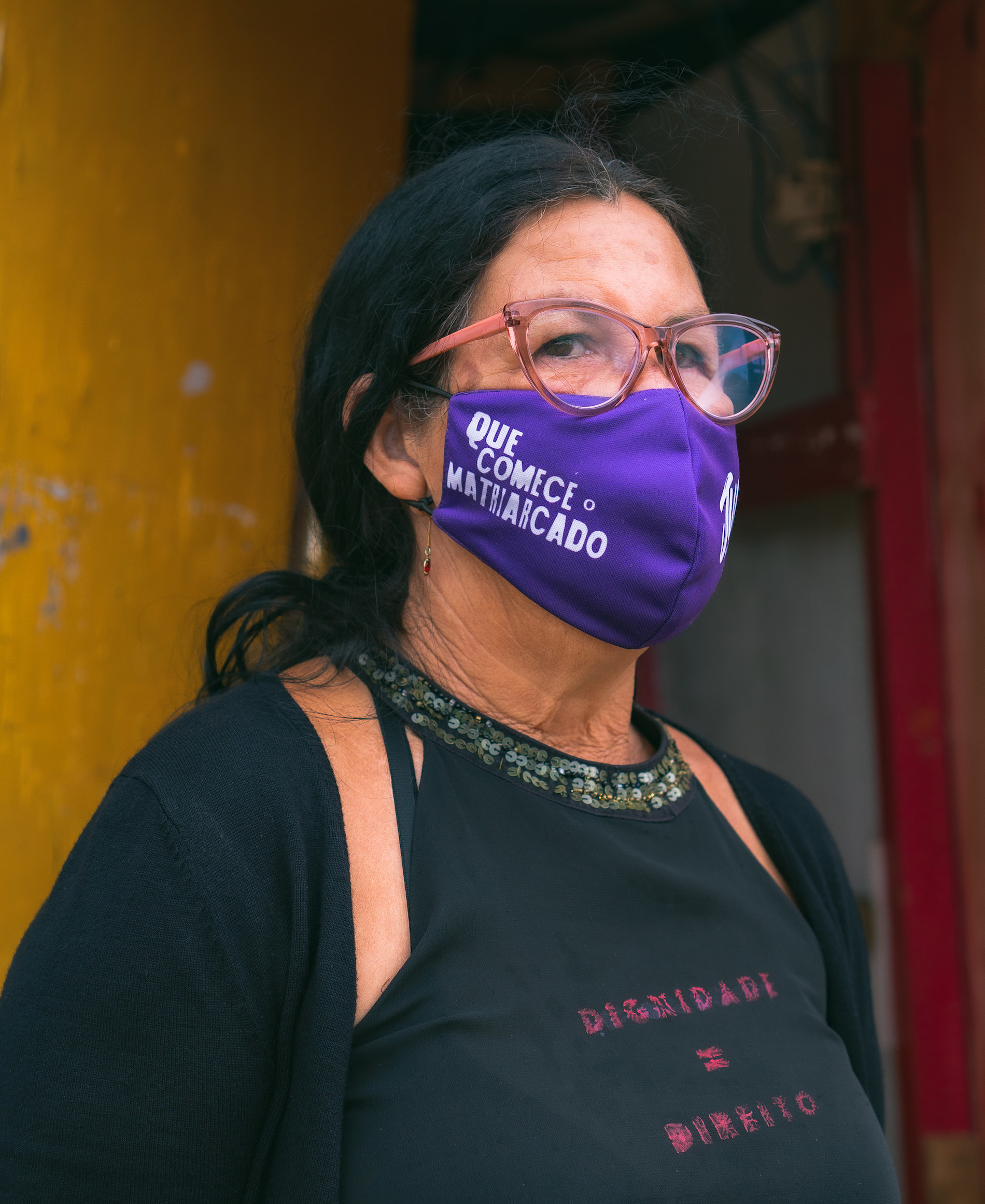 Dona Cigana, moradora da ocupação, vestindo uma camiseta preta onde se lê Dignidade = Direito e uma máscara rosa escrito Que Comece o Matriarcado.