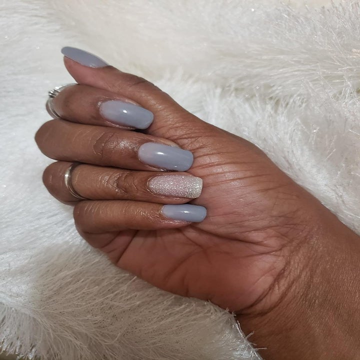 Reviewer with periwinkle nails and glittery white accent nail