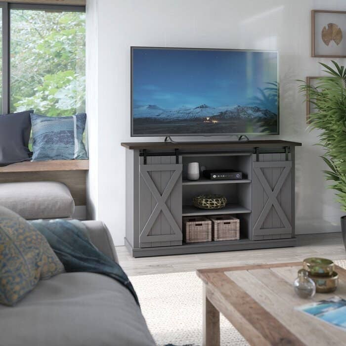 gray tv stand with sliding doors holding up a TV and displaying a vase and basket in the front