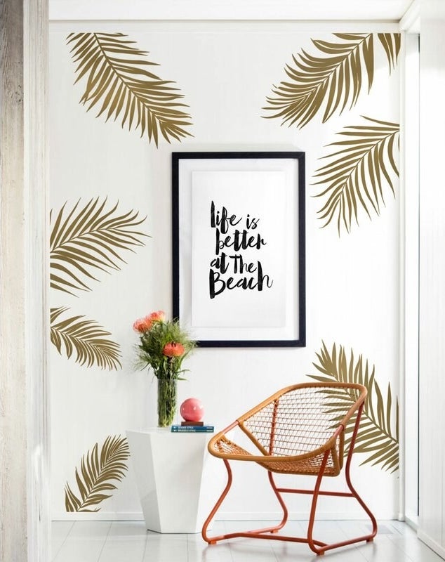 A white wall with seven giant gold palm leave stickers behind a chair and side table