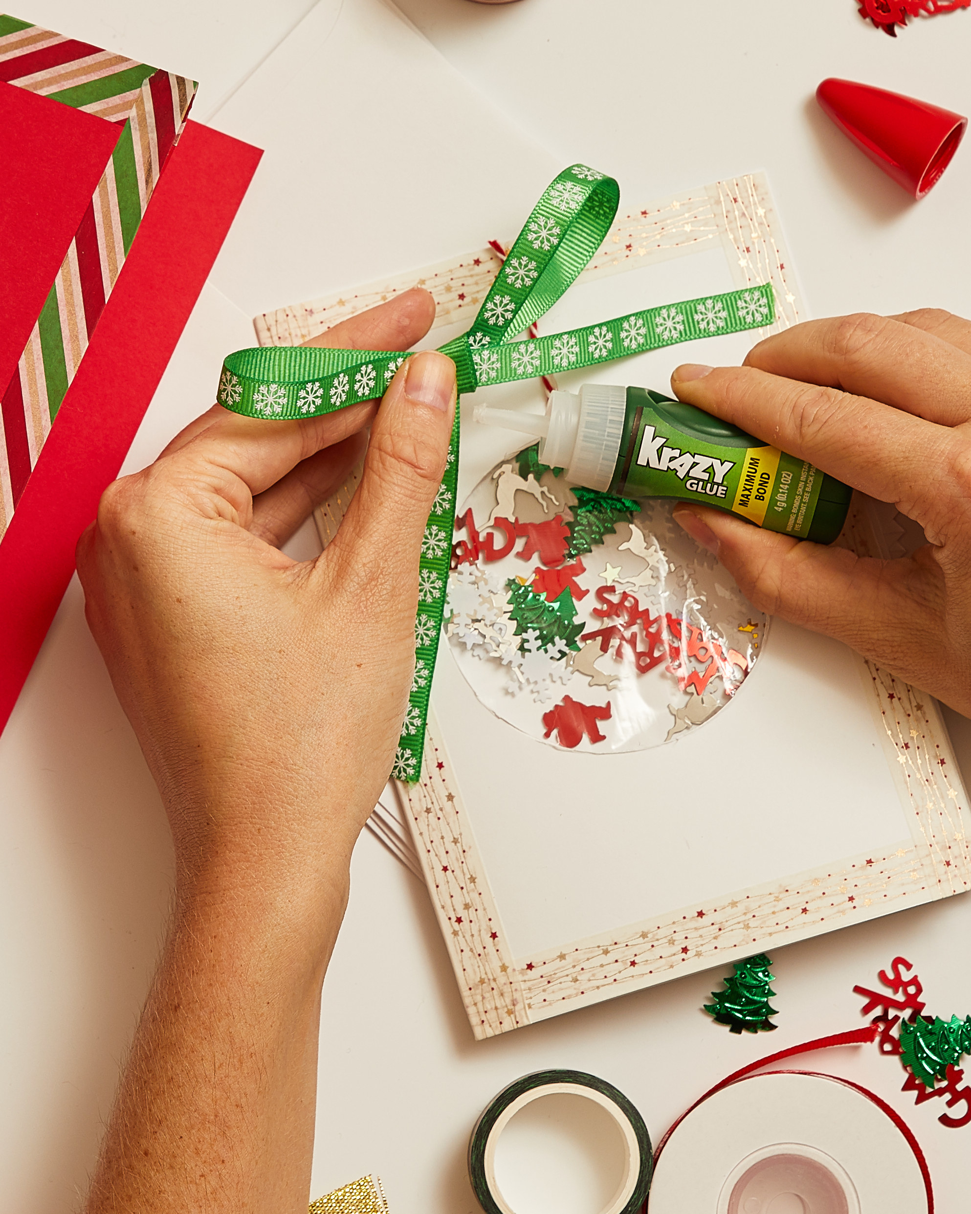 Person gluing a bow to the top of the card over the ornament.