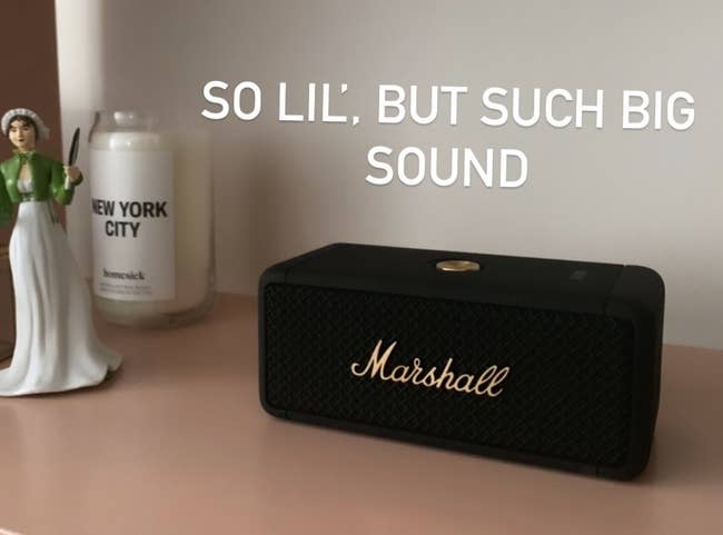 The black rectangular speaker that's shorter than a candle on a bookshelf with gold lettering that says Marshall