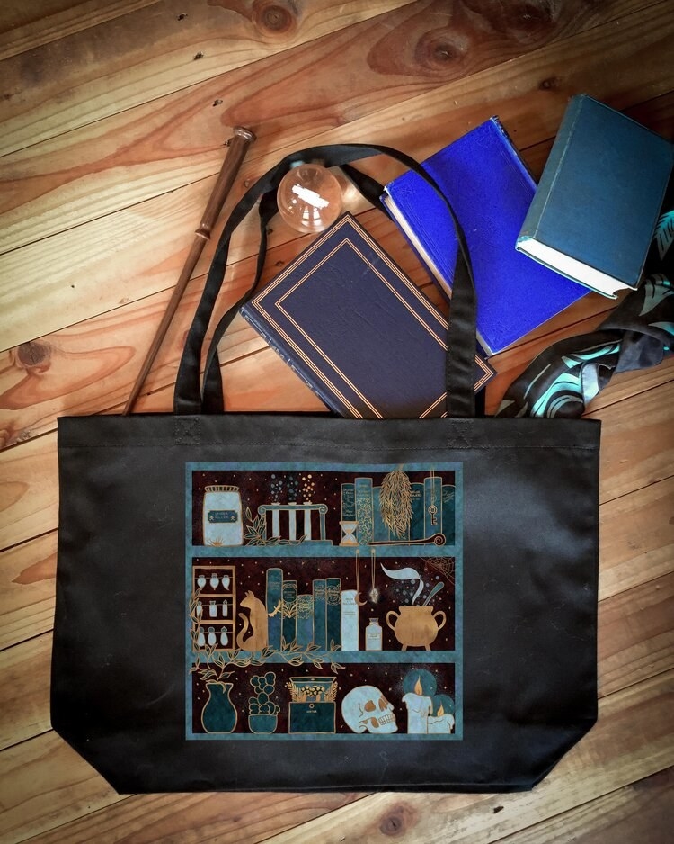 The black tote with an illustration of shelves holding books, a skull, a cauldron, candles, plants, and potions