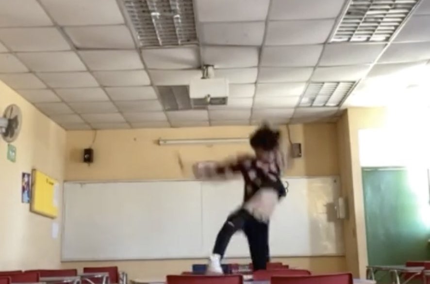 A man appears to fall off of a classroom desk