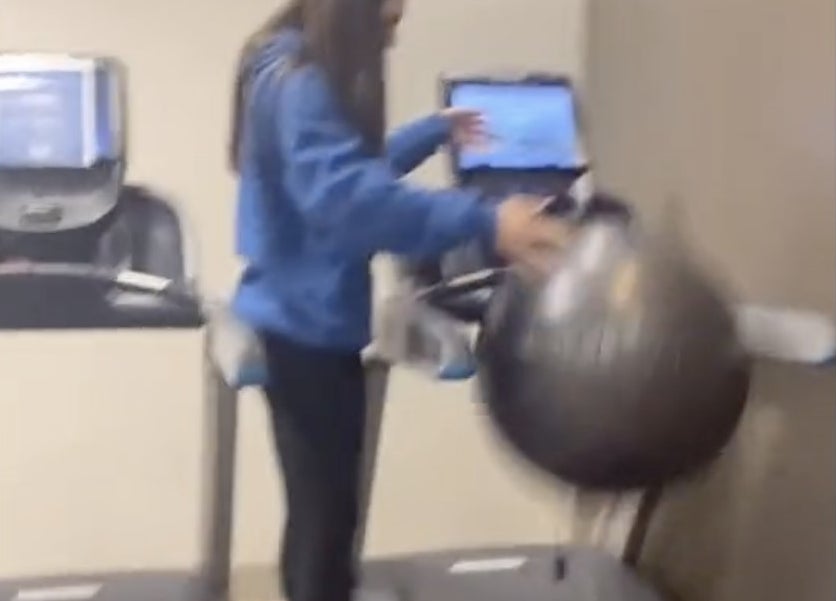 A woman stands on a treadmill with an exercise ball