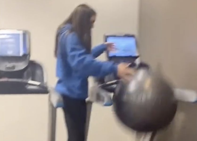 A woman stands on a treadmill with an exercise ball