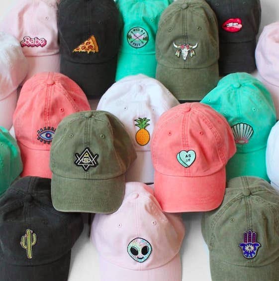 Pink, black, and green baseball caps with different patches on the front