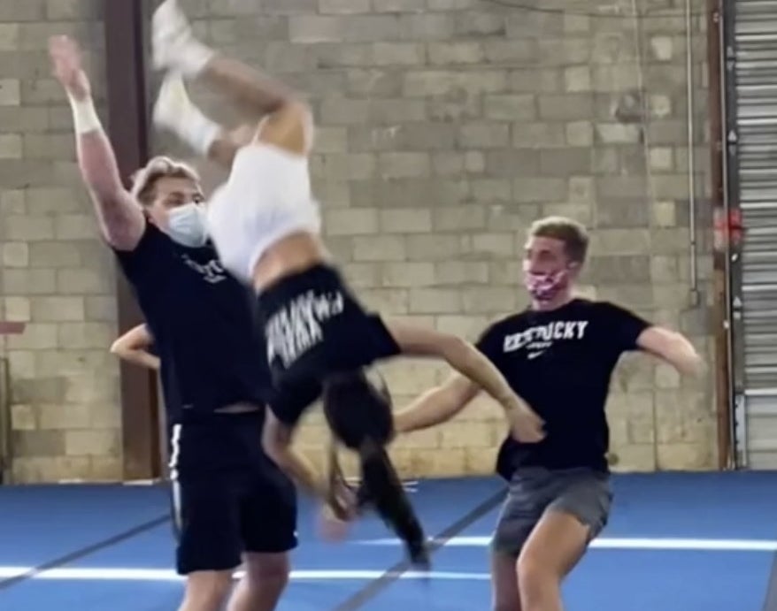 A cheerleaders flies through the air after two men fail to catch her