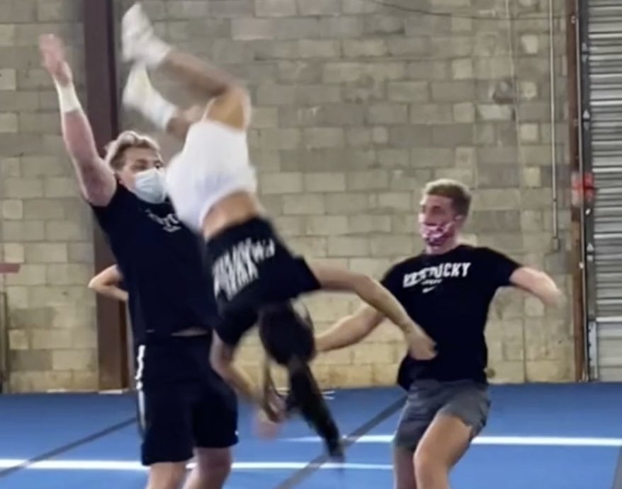 A cheerleaders flies through the air after two men fail to catch her