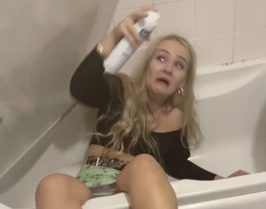 A woman sits in a bathtub as the glass door falls down