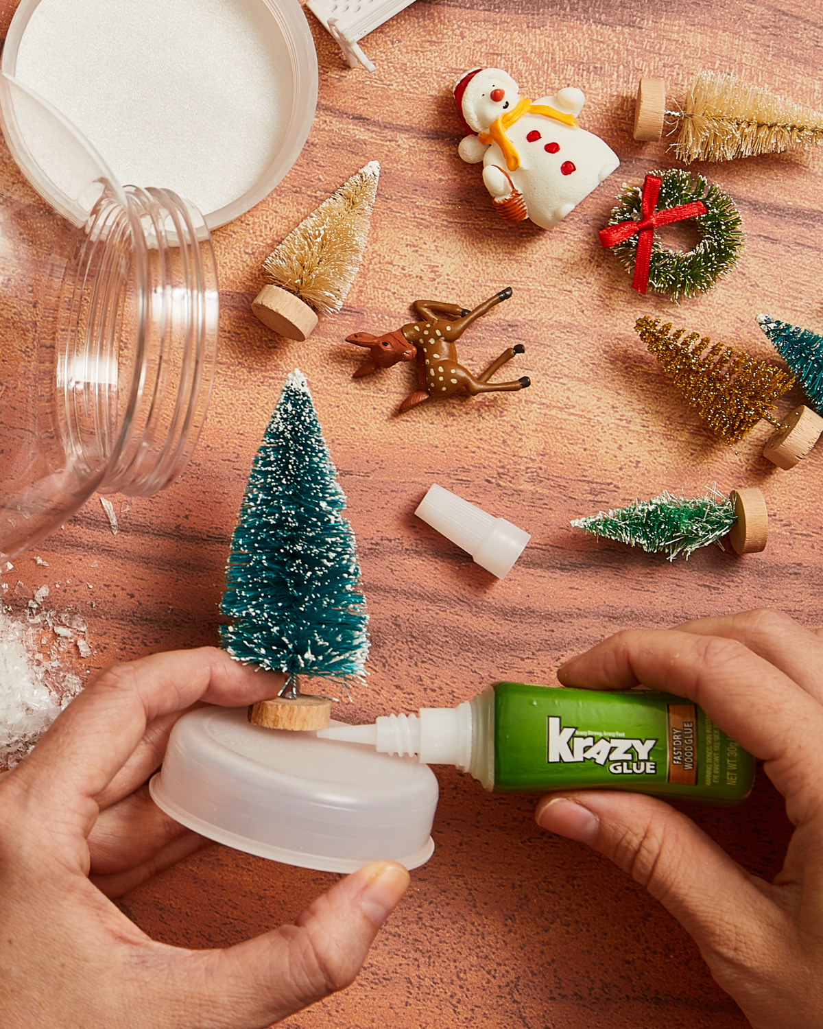 Person Krazy Gluing miniature tree to the platform of a craft snow globe.