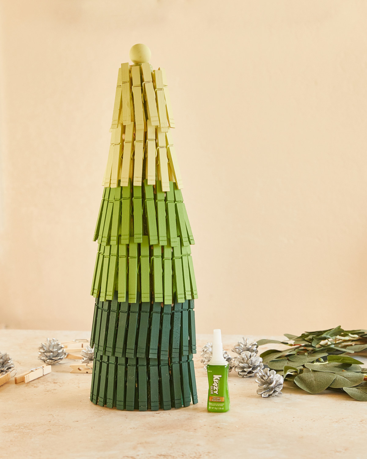 Completed clothespin tree with dark and light green clothespins. Bottle of Krazy Glue off to the side.