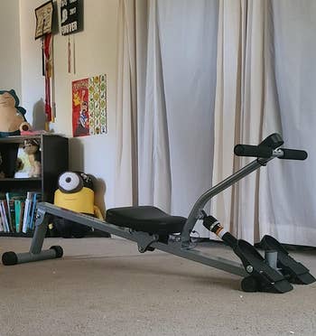 Reviewer pic of the small rowing machine in dark gray with black seat, food holders, and arm rest