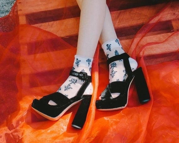 Model wears white sheer socks with a floral pattern under a pair of velvet open-toe platform shoes