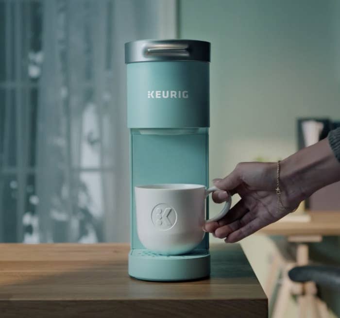 Person is holding a cup on a mint blue single cup Keurig