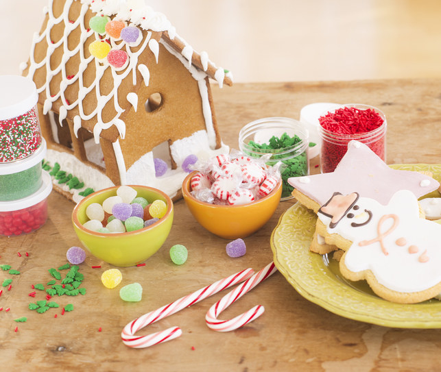 A gingerbread house decorated and held together with frosting surrounded by candy and snowman-shaped cookies