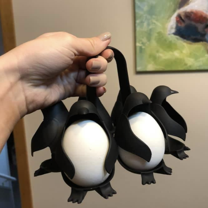 Hand holding penguin-shaped egg cooker with eggs sitting in the penguins bellies