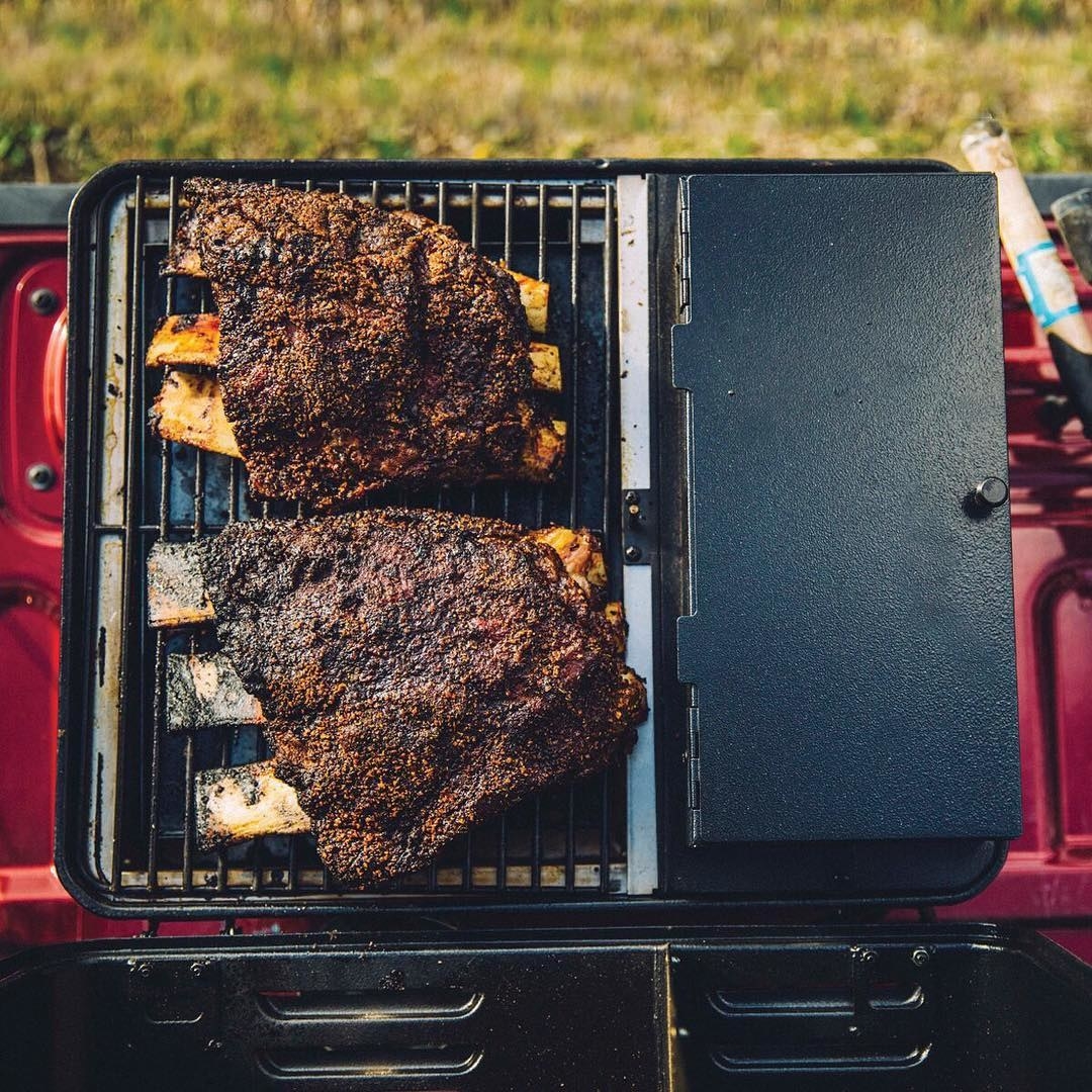 The portable grill set up on truck bed with large ribs cooking