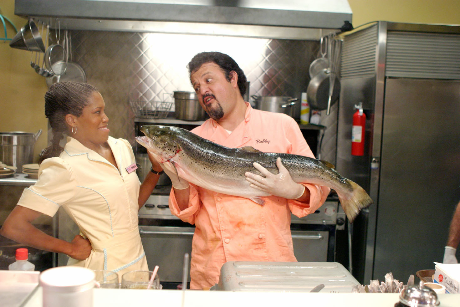 Bobby putting a big fish near Rhonda&#x27;s face in the kitchen of the diner