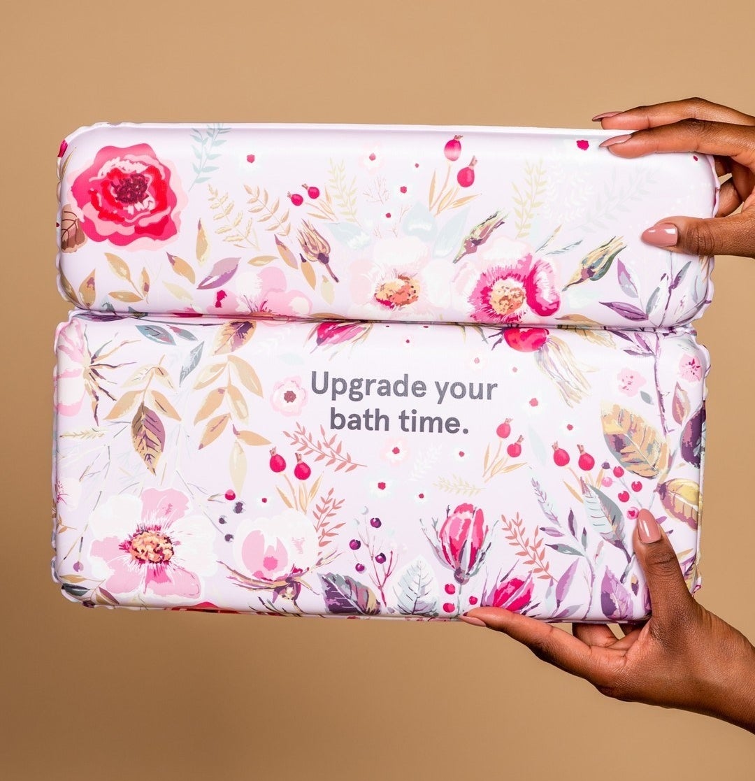 A person off-camera holding up the floral-printed rectangular bath pillow