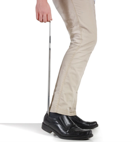 A person uses the shoe horn to put on a pair of leather loafers