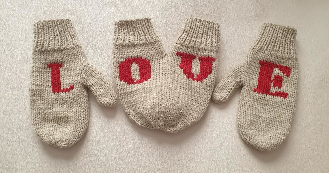 Two regular mittens and one set of hand holding mittens, spelling out the word LOVE