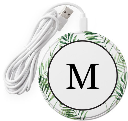 a round wireless charger with palm leaves around the edges and an M in the middle