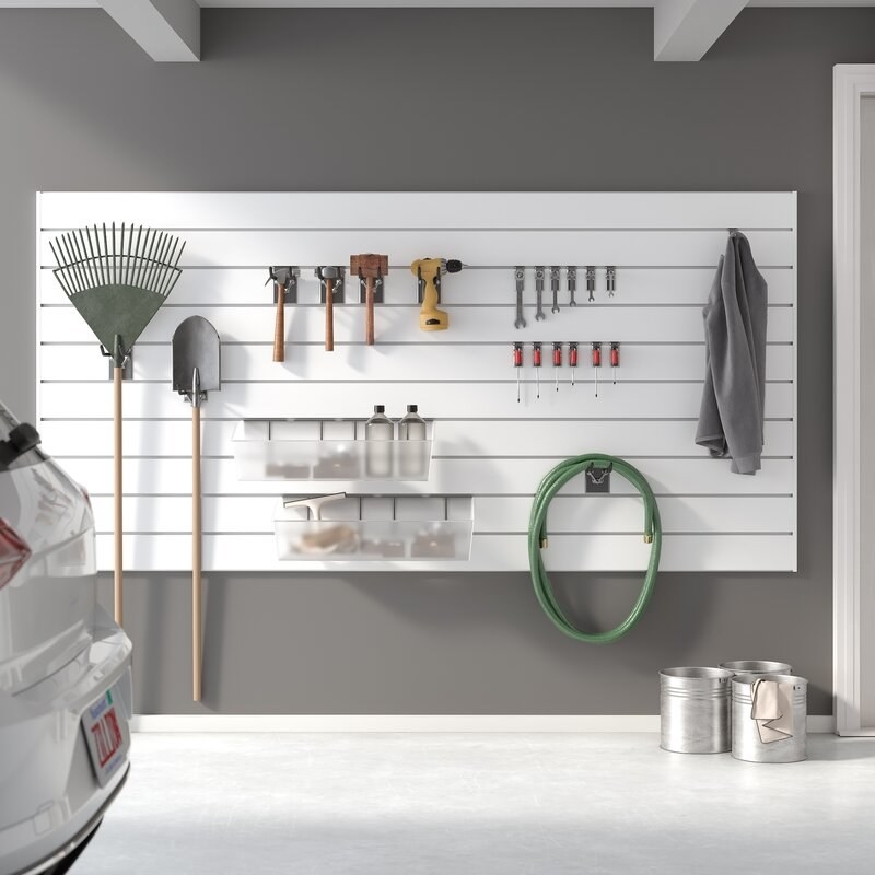 The white slatwall mounted to a garage wall and holding a variety of tools