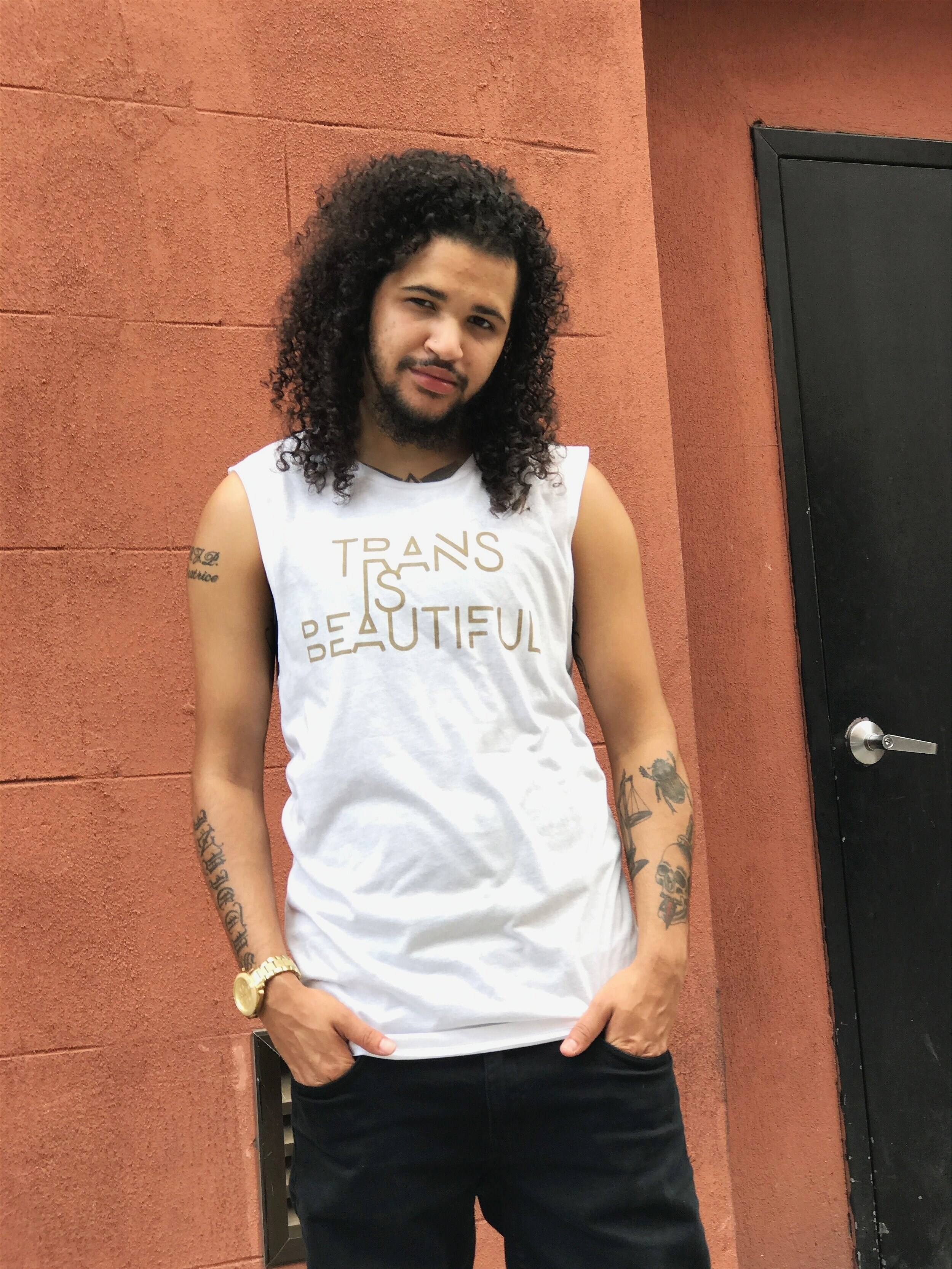 a model wearing the muscle tank that says &quot;trans in beautiful&quot; in gold lettering 