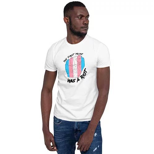 a model wearing the T-shirt with a blue, pink, and white fist surrounded by the words &quot;the first pride was a riot&quot;