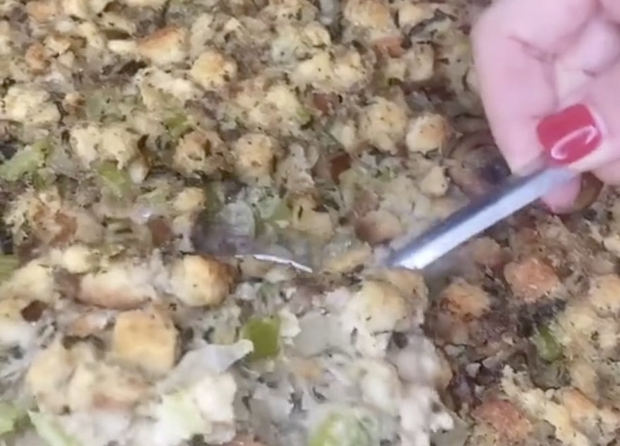 A spoon dips into a pan filled with stuffing