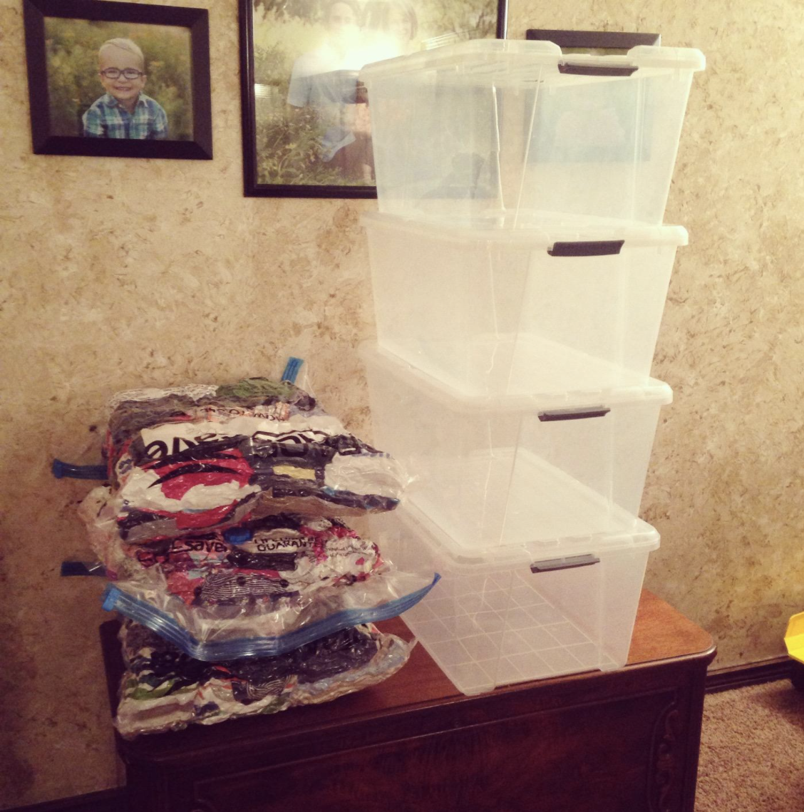 Three space saver bags next to four stacked plastic containers to illustrate the difference in size showing how much space the bags can save as the stack of bags were significantly smaller than the stack of plastic bins