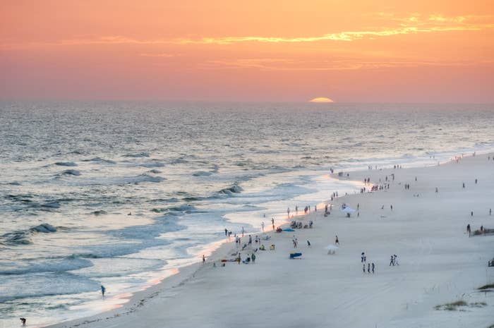 Orange beach&#x27;s white sand and blue waters at sunset, dotted with people